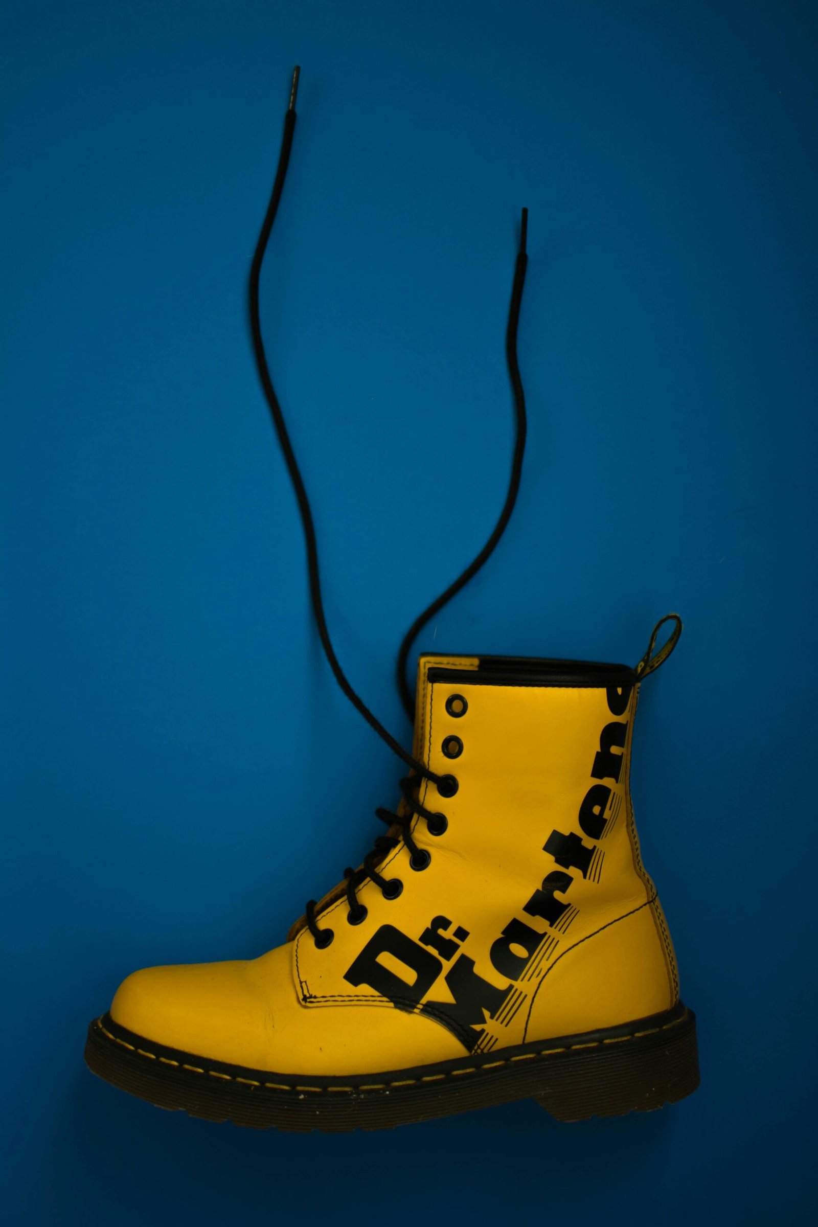 Eye-catching yellow Dr. Martens boot with laces on a bold blue background.