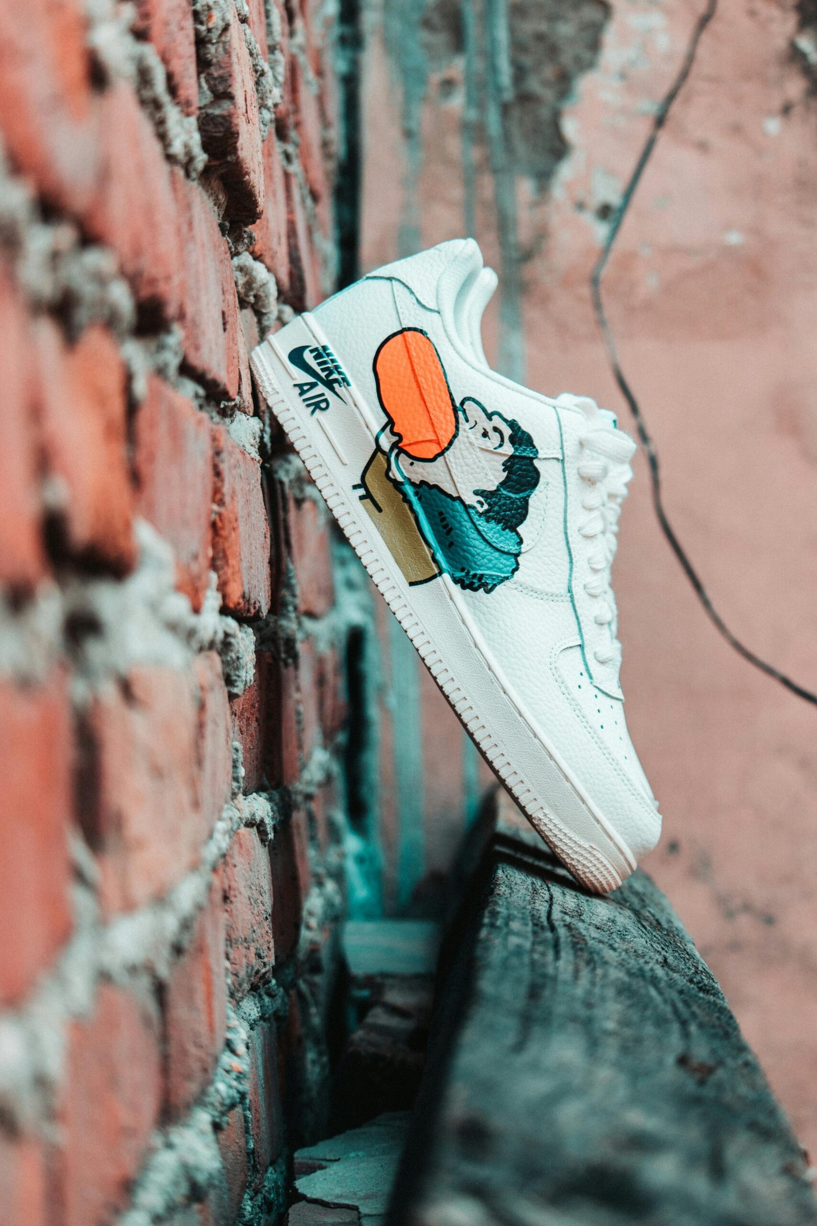 White Nike sneakers with cartoon design against a rough brick wall in urban setting.
